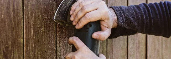 Person schleift Holzzaun mit Schleifgerät